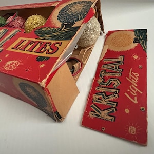 May include: A vintage box of red and white Christmas lights with the text "Kristal Lights" on the side. The box is open and shows the lights inside, which are white and have a frosted finish.