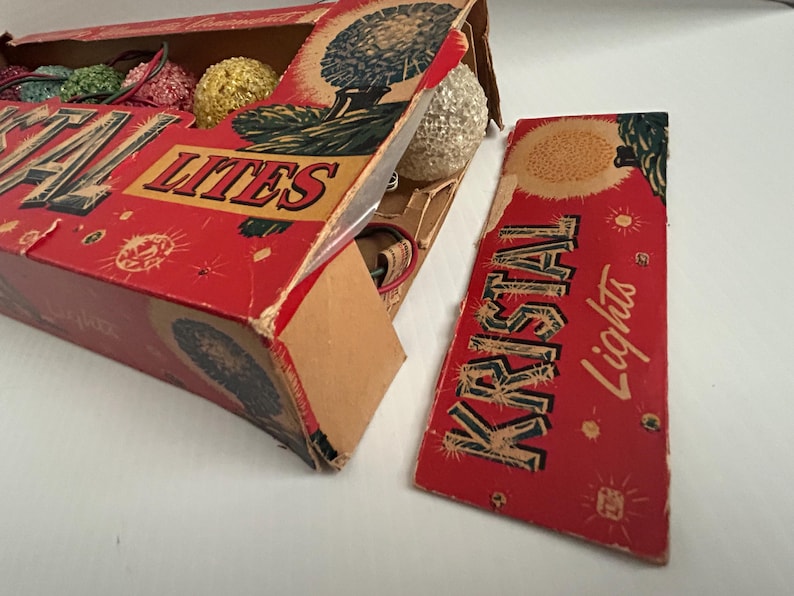 May include: A vintage box of red and white Christmas lights with the text "Kristal Lights" on the side. The box is open and shows the lights inside, which are white and have a frosted finish.
