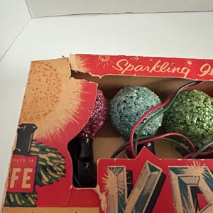 May include: A box of vintage Christmas lights with a red, green, and pink bulb. The box is labeled "Sparkling Illum"