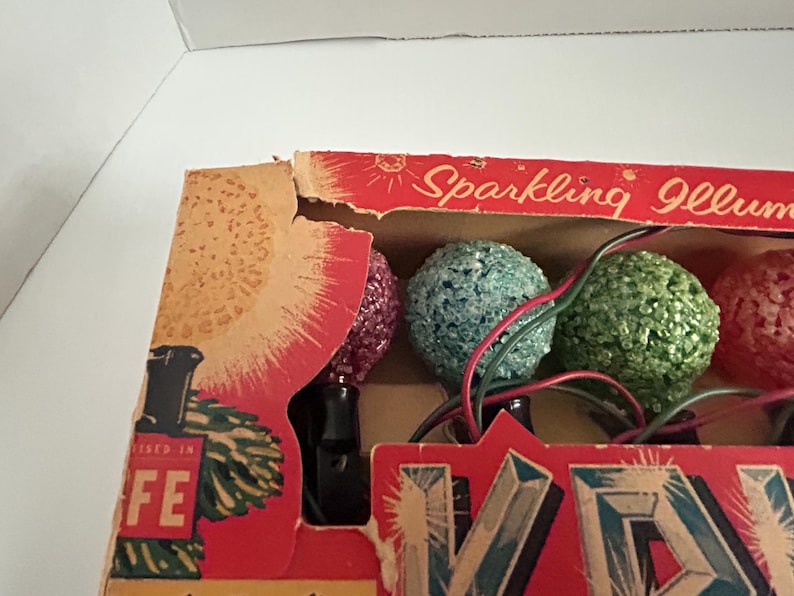 May include: A box of vintage Christmas lights with a red, green, and pink bulb. The box is labeled "Sparkling Illum"