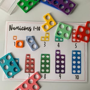 May include: A set of colourful plastic Numicon tiles for learning maths. The tiles are numbered 1 through 10 and are arranged in a row on a white background. The tiles are shaped like different geometric figures, with the number of holes in each tile corresponding to the number it represents.