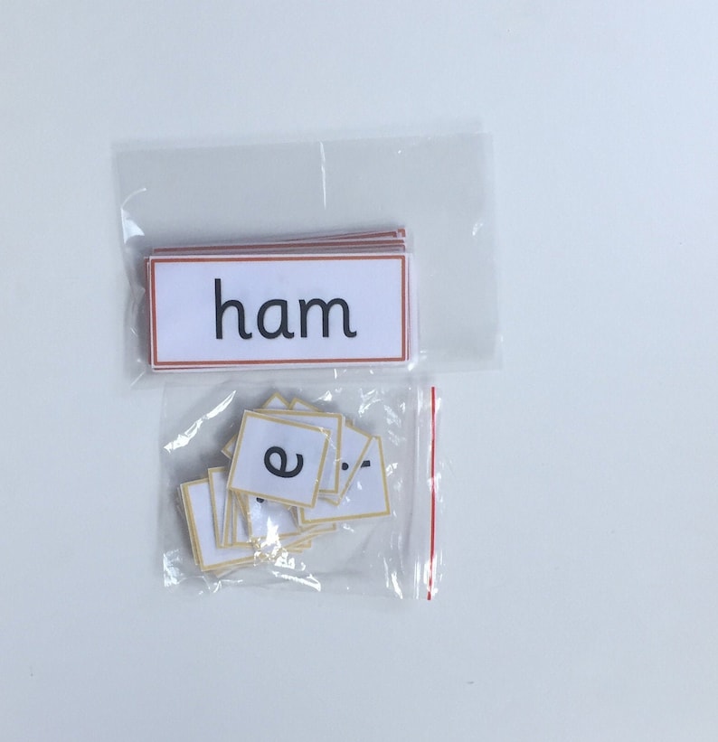 May include: A clear plastic bag containing a stack of white cards with the word "ham" printed in black on a red background. A second clear plastic bag contains a stack of white cards with the letter "e" printed in black on each card.