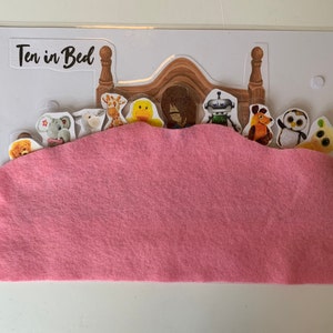 May include: A pink felt bed with a white background and the words "Ten in Bed" printed on the top. There are ten characters in the bed, including a robot, a giraffe, a teddy bear, a penguin, and a yellow alien.