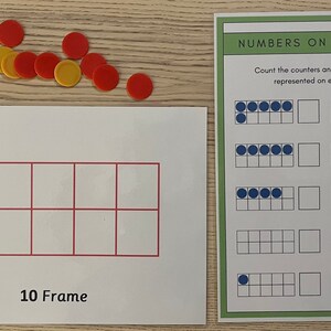 May include: Educational math materials including a 10 Frame card and a worksheet titled "NUMBERS ON A 10 FRAME". The worksheet has ten frames with blue counters. Red and yellow counters are scattered on the wooden surface.