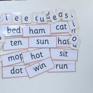May include: A set of white flashcards with black text, featuring common sight words for early readers. The words include "bed", "ham", "ten", "sun", "mop", "hot", "dot", "win", "cat", "hat", "sit", "run".