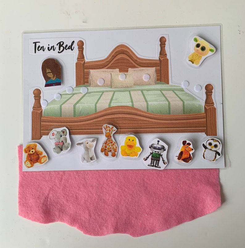 May include: A felt play set with a wooden bed and various animal and toy characters. The set includes a sheep, a giraffe, a duck, a robot, a bear, a donkey, an elephant, an owl, and a dog. The set is titled "Ten in Bed".