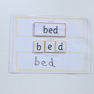 May include: A white card with the word "bed" written in three different ways. The first way is in red letters, the second way is with letter tiles, and the third way is handwritten.
