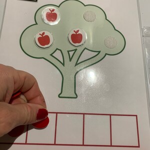 May include: A green tree with three red apples and three white circles. The number 3 is written in a black square at the top of the image. There are four empty red squares below the tree.
