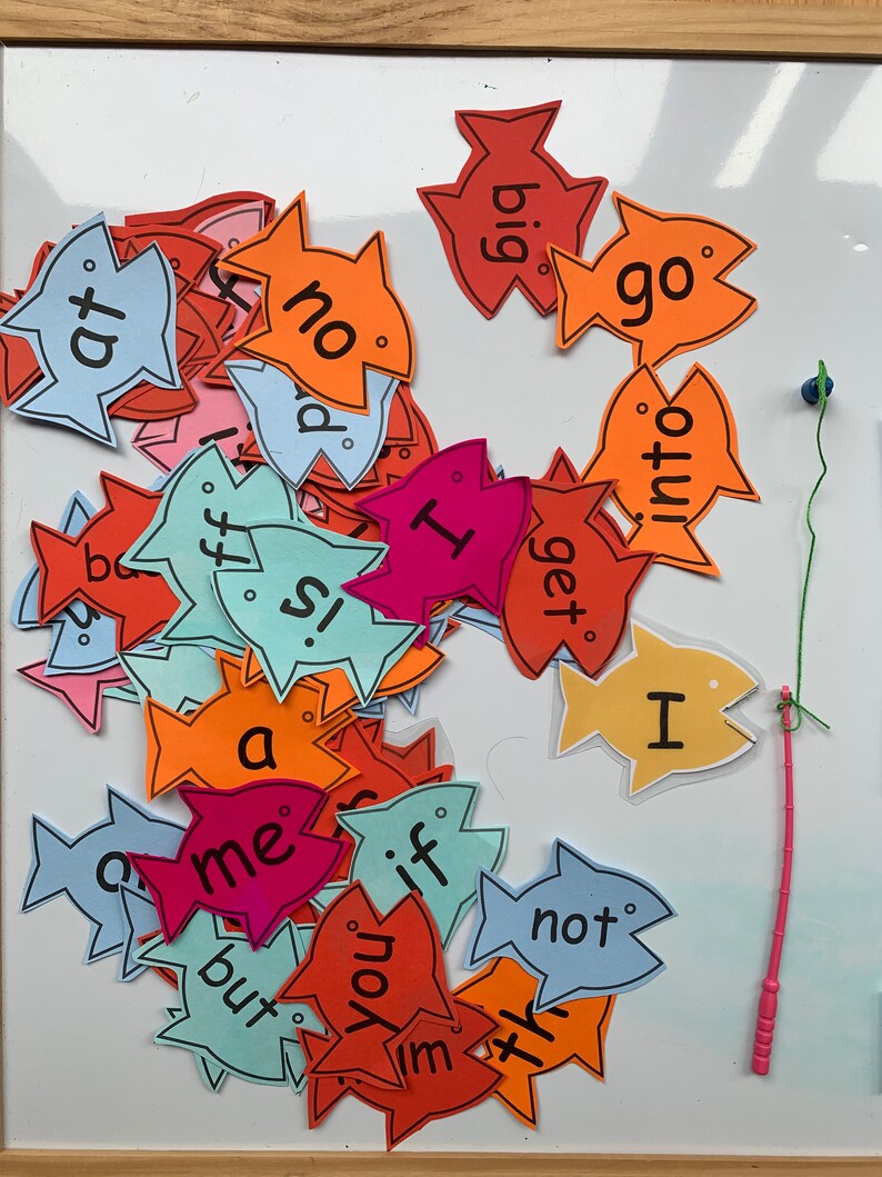 May include: A collection of colourful fish-shaped cards with words written on them, including "at", "no", "big", "go", "ff", "is", "me", "but", "if", "you", "im", "x", "not", "I", "get", "into".