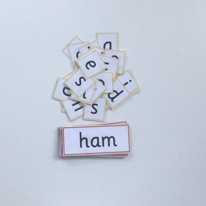 May include: A pile of white letter tiles with yellow borders, spelling out the word "ham" on a white surface.