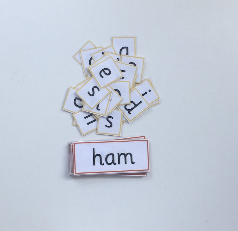May include: A pile of white letter tiles with yellow borders, spelling out the word "ham" on a white surface.