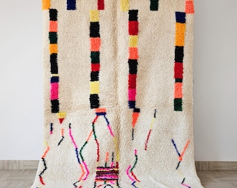 Peut inclure: Un tapis rectangulaire crème avec une surface texturée. Des colonnes verticales de carrés colorés orange, noirs, rouges et jaunes sont présentes. Le bas présente un motif géométrique avec des lignes colorées et des glands.