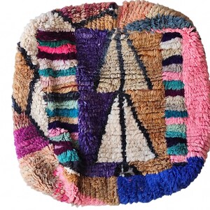 Puede incluir: Una colorida alfombra cuadrada de estilo marroqu&iacute; con un dise&ntilde;o de patchwork. La alfombra presenta una variedad de colores, incluyendo rosa, morado, azul y beige. El n&uacute;mero "8" est&aacute; en la esquina superior izquierda. La alfombra tiene una apariencia texturizada y tejida.