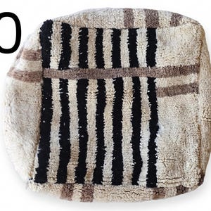 Puede incluir: Un puf cuadrado y texturizado con un fondo color crema y rayas negras verticales. El puf tambi&eacute;n presenta rayas marrones y el n&uacute;mero "10" en negro en la esquina superior izquierda. Este art&iacute;culo decorativo es adecuado para la decoraci&oacute;n del hogar.