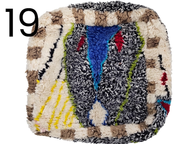 Puede incluir: Una alfombra cuadrada y texturizada con un dise&ntilde;o abstracto y colorido. La alfombra presenta una mezcla de blanco, negro, azul, rojo, amarillo y verde. El n&uacute;mero "19" est&aacute; en la esquina superior izquierda.