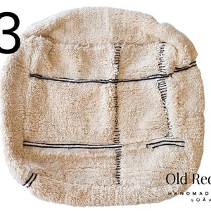 Puede incluir: Puf texturizado de color crema con l&iacute;neas cosidas negras. El puf tiene forma cuadrada con esquinas redondeadas. El n&uacute;mero 13 est&aacute; en la esquina superior izquierda. Las palabras "Old Red City" y "Handmade with Loave" est&aacute;n en la esquina inferior derecha.