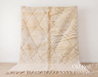Op de afbeelding: Een beige Marokkaans tapijt met een ruitpatroon. Het tapijt heeft een dikke, getextureerde pool en een franje langs de onderrand. Het tapijt wordt tegen een witte muur getoond. De tekst "Old Red City" is zichtbaar.
