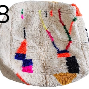Puede incluir: Alfombra redonda, texturizada, de color blanquecino con dise&ntilde;os geom&eacute;tricos coloridos. La alfombra presenta formas naranjas, azules, rosas, amarillas, verdes y negras. El n&uacute;mero "18" est&aacute; en la esquina superior izquierda.