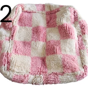 Puede incluir: Un coj&iacute;n cuadrado y afelpado con un dise&ntilde;o de tablero de ajedrez rosa y blanco. El coj&iacute;n tiene un aspecto suave y texturizado y probablemente est&aacute; hecho de un material esponjoso. El n&uacute;mero "22" est&aacute; en la esquina superior izquierda.
