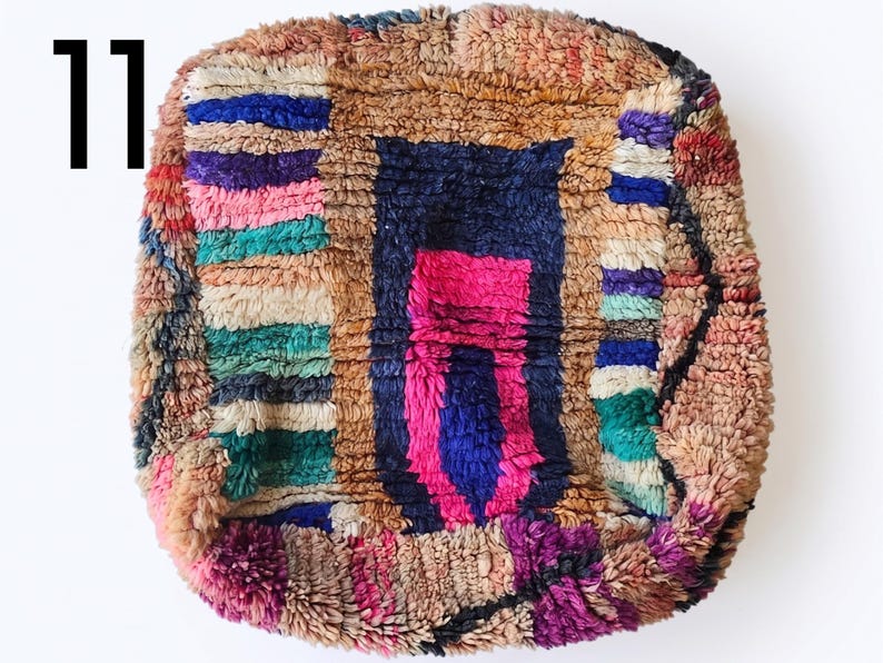 Puede incluir: Un coj&iacute;n de suelo colorido y texturizado con un dise&ntilde;o geom&eacute;trico. El coj&iacute;n presenta una forma central azul oscuro con un acento rosa, rodeada por un borde marr&oacute;n y rayas coloridas. El n&uacute;mero "11" est&aacute; en la esquina superior izquierda.