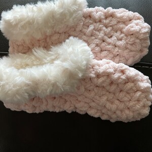 May include: A pair of pink fuzzy slippers with white faux fur trim. The slippers are crocheted and have a soft, cozy texture.