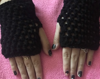 May include: A pair of black crocheted fingerless gloves with a square pattern. The gloves are on a pink fuzzy surface.