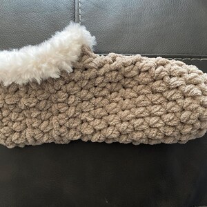 May include: A pair of cozy brown crocheted slippers with a white faux fur trim. The slippers are made with a chunky yarn and have a soft, comfortable texture.