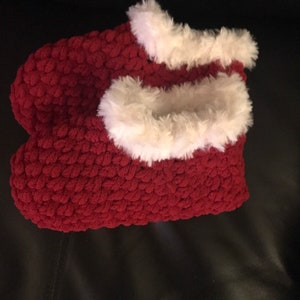 May include: A pair of red fuzzy slippers with white faux fur trim. The slippers are made of a soft, plush material and are perfect for keeping your feet warm in the winter.