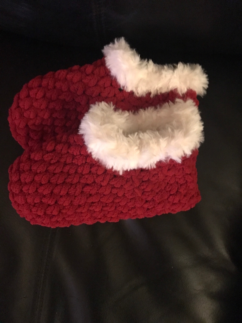 May include: A pair of red fuzzy slippers with white faux fur trim. The slippers are made of a soft, plush material and are perfect for keeping your feet warm in the winter.
