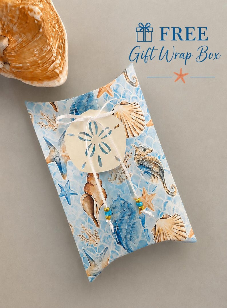 May include: A rectangular pillow box with a light blue background featuring a pattern of seashells, starfish, and seahorses. A white string ties a sand dollar cutout to the center, accented with small blue and gold beads. Text reads FREE Gift Wrap Box.