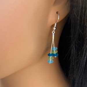 May include: A dangle earring featuring a silver-toned hook and two thin silver chains. The chains are adorned with five small, frosted, round beads in alternating shades of light blue, lime green, and dark blue, creating a layered effect.