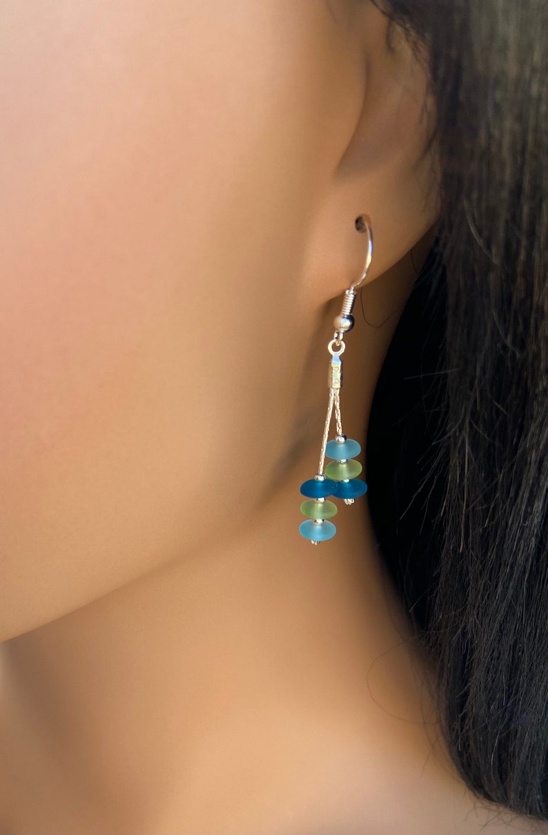 May include: A dangle earring featuring a silver-toned hook and two thin silver chains. The chains are adorned with five small, frosted, round beads in alternating shades of light blue, lime green, and dark blue, creating a layered effect.
