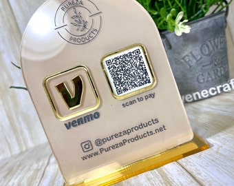 May include: A clear acrylic display stand with a peach-coloured face and a gold-coloured base. The stand features a Venmo logo and a QR code with the text "scan to pay". The Pureza Products logo and social media information are also displayed.