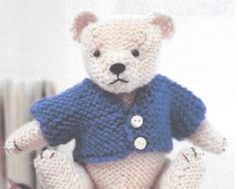 May include: A knitted teddy bear wearing a blue cardigan with white buttons. The bear is sitting on a white surface.