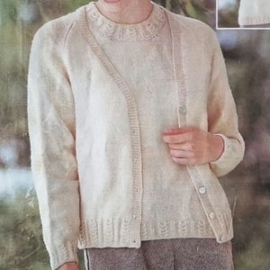 May include: A white knitted cardigan with a v-neck and button closure. The cardigan is worn over a white knitted top with a lace trim.