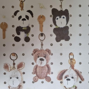 May include: A collection of handmade keychains featuring various animal designs. The keychains include a panda, a bear, a bunny, a dog, and a bear. Each keychain is attached to a metal ring and includes a key.