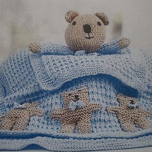 May include: A light blue knitted baby blanket featuring three teddy bear appliqués. A matching teddy bear head is at the top. The teddy bears are tan, and the blanket is a soft, textured knit, perfect for a newborn.