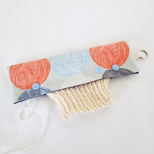 May include: A beige knitted yarn bowl with a fabric cover featuring a pattern of colourful yarn balls. The cover has blue buttons and a loop for hanging.