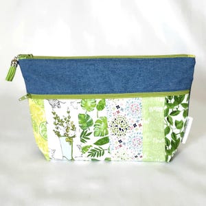 May include: A zipped pouch featuring a blue denim upper section and a multi-patterned lower section with green, white, and yellow botanical and cat prints. The bag includes a lime green zip and a matching green tassel attached to the zip pull.