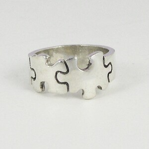 May include: A silver ring with a puzzle piece design. The ring is made of multiple puzzle pieces that fit together to form a continuous band.