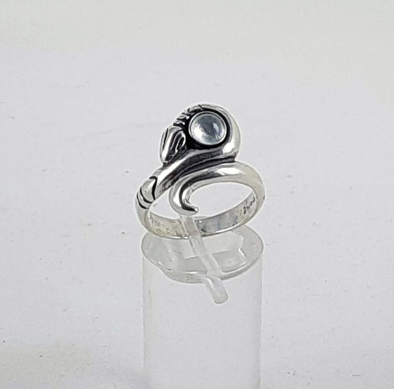 May include: A silver ring featuring a snake design with a clear gemstone. The snake's head is raised and the gemstone is set in the snake's eye.