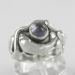 Peut inclure: Une bague en argent avec un design abstrait orné d'une pierre précieuse violette. La bague est en argent sterling et a une forme unique et organique.