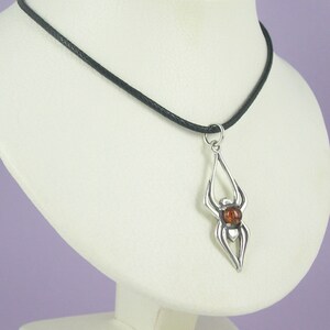 May include: A silver spider pendant with an amber gemstone in the centre, hanging from a black cord necklace.