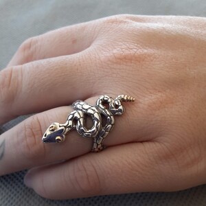 May include: A silver snake ring with gold accents. The snake is coiled around the finger and has a detailed, textured design.