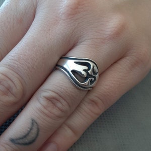 May include: A silver ring with a decorative design on the band. The design is a stylized floral pattern.