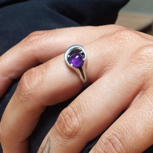 May include: A silver ring with a purple amethyst gemstone set in a unique, curved design.