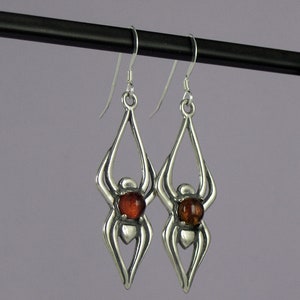 May include: Silver spider earrings with amber gemstones. The earrings are dangle style and have a delicate design.