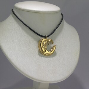 May include: A gold pendant necklace with a crescent moon design. The pendant features a stylised figure holding the moon in their hands.
