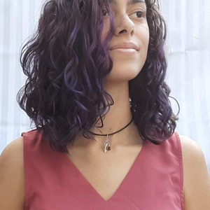 May include: A person with long, curly, purple hair wearing a red sleeveless top and a silver choker necklace with a small pendant.