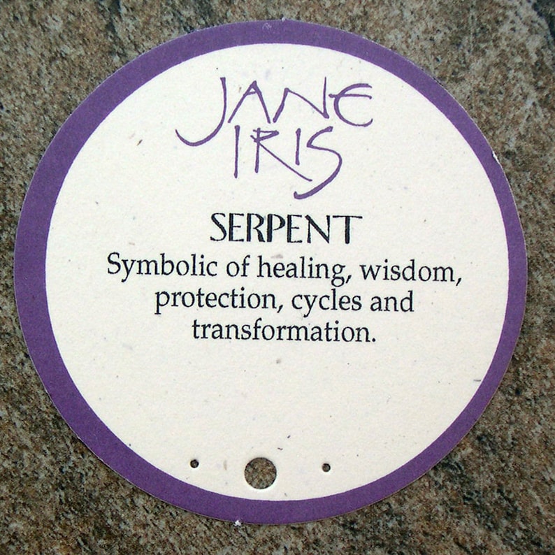 May include: A round, purple-bordered tag with the text "JANE IRIS" and "SERPENT" in black. The tag also includes the text "Symbolic of healing, wisdom, protection, cycles and transformation."